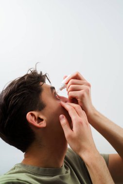 Adam alerji tedavisi için göz damlası kullanıyor. Adamın gözü tahriş sorunu yüzünden damlıyor. Evde göz damlası kullanılıyor.