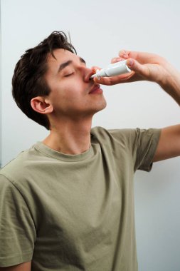 Hasta beyaz arka planda sinüzit tedavisi için burun damlası alıyor. Adam grip için burun spreyi kullanıyor.