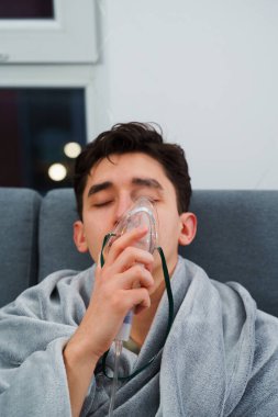 Evde öksürük tedavisi için nebulizör maskesiyle hava solumak. Hasta adam nebulizatörle solunum tedavisi görüyor.