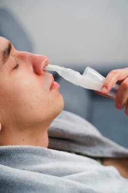 Evde nebulizörle burun solumuş. Astım krizi geçirmiş genç bir adam solunum cihazıyla nefes alıyor.
