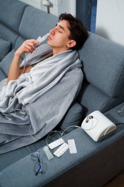 Evde nebulizörle burun solumuş. Astım krizi geçirmiş genç bir adam solunum cihazıyla nefes alıyor.