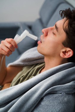 Evde nebulizatörün yardımıyla ağız solunumu. Hasta adam evde grip tedavisi için ağız spreyi nebulizatörü kullanıyor.