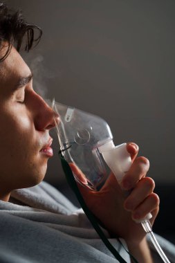 Öksürük tedavisi için oksijen maskesi yutan bir adam. Evde hastalık tedavisi için kompresör nebulizörü kullanılıyor.