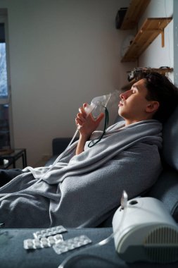 Öksürük tedavisi için oksijen maskesi yutan bir adam. Evde hastalık tedavisi için kompresör nebulizörü kullanılıyor.