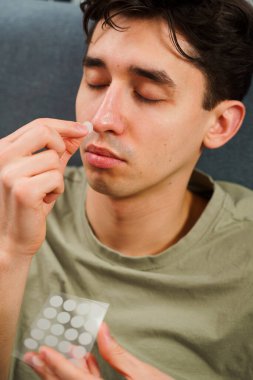 Cilt bakımı için sivilce bandı kullanıyorum. Genç adam sivilceleri temizlemek için alnına sivilce bandı yapıştırıyor.