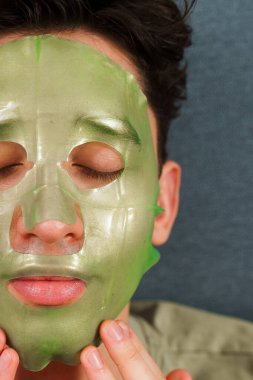 İnsan cildini yenilemek için maske takıyor. Cilt bakımı için. Evde yüz maskesi takmış rahat bir adam var.