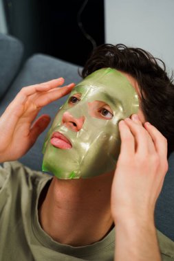 İnsan cildini yenilemek için maske takıyor. Cilt bakımı için. Evde yüz maskesi takmış rahat bir adam var.