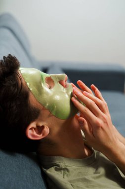 Derisini sulandırıcı ve nemlendirici yüz maskesi ile besleyip şımartıyor. Genç adam susuzluk efektli yeşil yüz maskesi kullanıyor. Erkek güzellik prosedürleri