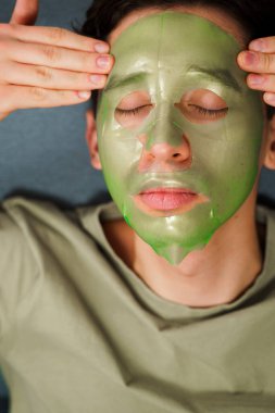 Derisini sulandırıcı ve nemlendirici yüz maskesi ile besleyip şımartıyor. Genç adam susuzluk efektli yeşil yüz maskesi kullanıyor. Erkek güzellik prosedürleri
