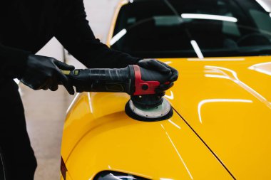 Araba servisinde yörünge cilası kullanarak sarı spor araba kaputunu cilalama işlemi. Yörüngesel cilalama ile cilalamak için aşındırıcı macun kullanılıyor.