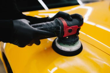 Yörünge cilasıyla cilalamak için aşındırıcı macun kullanılıyor. Araba servisindeki yörünge cilası makinesini kullanarak sarı spor araba kaput yüzeyinin cilalanması süreci ayrıntılandırılıyor