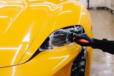 Araba farlarını köpük ve yumuşak fırçayla temizliyorum. Spor araba farlarını temizleme işlemi. Sabun köpüğü ve fırçayla yıkayın.