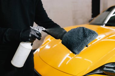 Araba temizleyicisi serviste mikrofiber beze ağda yapmak için sıvı püskürtüyor. Araba koruması için sprey ağda ürünü kullanma süreci ayrıntılandırılıyor