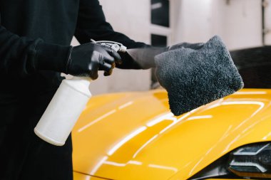 Araba temizleyicisi serviste mikrofiber beze ağda yapmak için sıvı püskürtüyor. Araba koruması için sprey ağda ürünü kullanma süreci ayrıntılandırılıyor