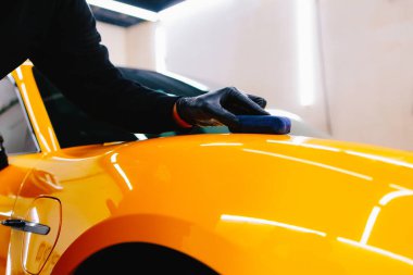Detaylı servis çalışanı spor arabaya seramik koruma sıvısı uygular. Sarı spor araba için koruyucu nano katman oluşturmak için seramik sıvıyı karıştırmak