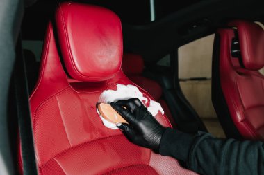 Araba yıkamada sabun köpüğüyle deri oto koltuğu temizleme işlemi. Adam arabanın kırmızı deri koltuğuna köpük sürüyor. Servis içi temizlik için.