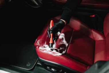 Adam, serviste detaylı işlem sırasında deri koltuğu köpük ve fırçayla temizliyor. İşçi, deri oto koltuğu için temizlik solüsyonu ve yumuşak fırça kullanır