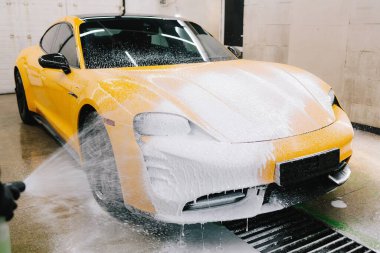İşçi sabun solüsyonunu oto yıkama için yüksek basınçlı su jeti ile spreyliyor. Spor araba temizliği için yüksek basınçlı su tabancası olan sabunlu köpük uygulaması.