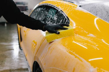 Araba yıkama servisinde köpük ve sarı süngerli deterjan kullanarak el yıkama. Otomobil servisinde köpüklü spor araba detaylandırılıyor