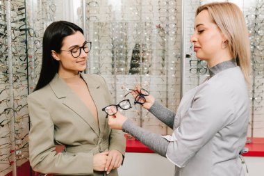 Oftalmolog hastanın doğru gözlüğü seçmesine yardım ediyor. Oftalmolog, gözlükçüdeki bir kadın müşteriye gözlük hakkında danışır.