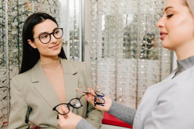 Oftalmolog hastanın doğru gözlüğü seçmesine yardım ediyor. Oftalmolog, gözlükçüdeki bir kadın müşteriye gözlük hakkında danışır.