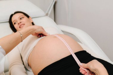 Jinekolog randevuda bebeğin büyümesini takip etmek için karnını mezurayla ölçüyor. Jinekolog klinikteki kadının karnının boyutunu kontrol ediyor.