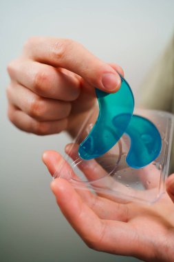 Erkek ellerinin elinde mavi bir kolajen pedi var. Cilt bakımı için yaşlanmayı önleyici nemlendirici göz maskesi