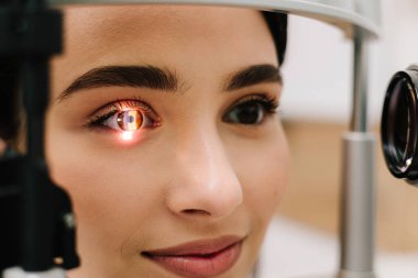 Kesik lambalı bir oftalmolog kadının gözlerini ve korneasını inceliyor. Göz doktoru, göz ve kornea teşhisi koymak için kesik lambadan gelen ışıkla hastanın gözünü aydınlatıyor.