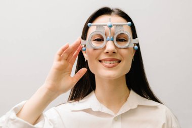 Kısa ya da uzun görüşlü bir kızın göz görme sistemini incelemek için deneme gözlüğü seçimi için oftalmolog muayenesi. Beyaz arka planda deneme çerçeveli gözlüklü kız