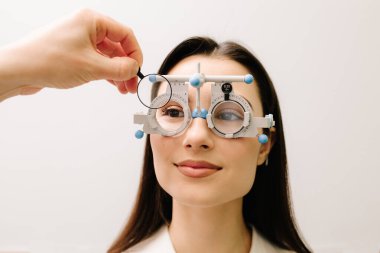 Kız göz muayenesi için göz doktorunun gözlük takıyor. Doğru reçeteli lensleri belirlemek için deneme çerçevesi gözlüğü