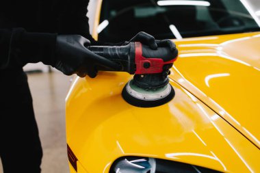 Yörünge cilasıyla cilalamak için aşındırıcı macun kullanılıyor. Araba servisindeki yörünge cilası makinesini kullanarak sarı spor araba kaput yüzeyinin cilalanması süreci ayrıntılandırılıyor