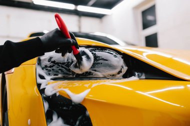 Spor araba farlarını temizleme işlemi sırasında sabun köpüğü ve fırçayla yıkanır. Araba farları köpük ve yumuşak fırçayla temizleniyor