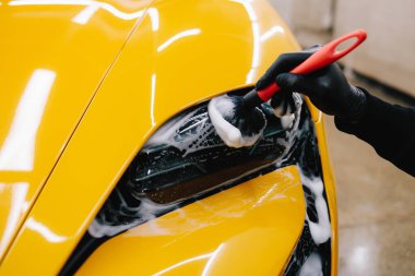 Araba farlarını köpük ve yumuşak fırçayla temizliyorum. Spor araba farlarını temizleme işlemi. Sabun köpüğü ve fırçayla yıkayın.