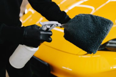 Araba temizleyicisi serviste mikrofiber beze ağda yapmak için sıvı püskürtüyor. Araba koruması için sprey ağda ürünü kullanma süreci ayrıntılandırılıyor