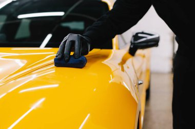 Detaylı servis çalışanı spor arabaya seramik koruma sıvısı uygular. Sarı spor araba için koruyucu nano katman oluşturmak için seramik sıvıyı karıştırmak