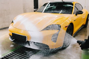 İşçi sabun solüsyonunu oto yıkama için yüksek basınçlı su jeti ile spreyliyor. Spor araba temizliği için yüksek basınçlı su tabancası olan sabunlu köpük uygulaması.