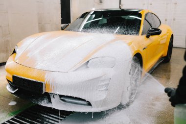 İşçi sabun solüsyonunu oto yıkama için yüksek basınçlı su jeti ile spreyliyor. Spor araba temizliği için yüksek basınçlı su tabancası olan sabunlu köpük uygulaması.