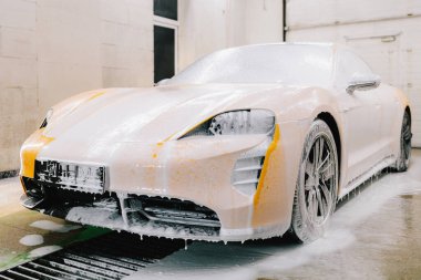 İşçi sabun solüsyonunu, araba yıkama için su jetinden gelen basınçla spreyliyor. Servisteki spor araba temizliği için sabunlu köpük uygulaması.