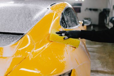 Araba yıkama servisinde köpük ve sarı süngerli deterjan kullanarak el yıkama. Otomobil servisinde köpüklü spor araba detaylandırılıyor