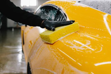 Araba yıkama servisinde sarı süngerli temizlikçi eli. Otomobil servisinde arabayı köpükle temizleme işlemi