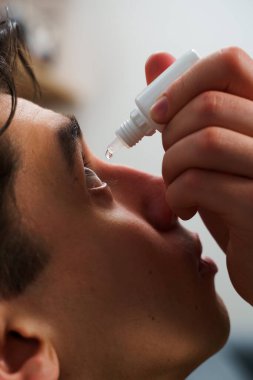 Adam evdeki göz sağlığından tıbbi göz damlası damlatıyor. Genç adam tahriş sorunu için göz damlası kullanıyor.