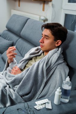 Adam üşümüş ve yatakta uzanıp burnunu burun spreyiyle siliyor. Adam burun spreyi kullanıyor ve hastalık tedavisi için ilaç ve ilaç alıyor.