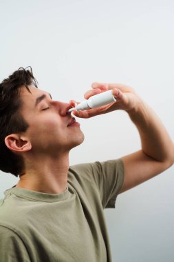 Adam grip için burun spreyi kullanıyor. Hasta beyaz arka planda sinüzit tedavisi için burun damlası alıyor.