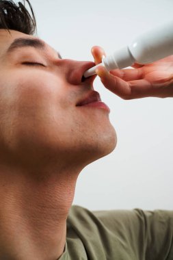Adam grip için burun spreyi kullanıyor. Hasta beyaz arka planda sinüzit tedavisi için burun damlası alıyor.