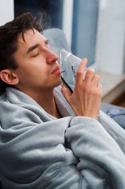 Hasta adam nebulizatörle solunum tedavisi görüyor. Evde öksürük tedavisi için nebulizör maskesiyle hava solumak