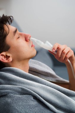 Astım krizi geçiren genç bir adam solunum cihazıyla nefes alıyor. Evde nebulizörle burun solumuş.
