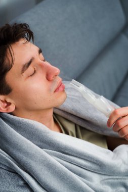 Astım krizi geçiren genç bir adam solunum cihazıyla nefes alıyor. Evde nebulizörle burun solumuş.