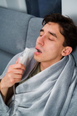 Hasta adam evde grip tedavisi için ağız spreyi nebulizatörü kullanıyor. Evde nebulizatörün yardımıyla ağız solunumu.