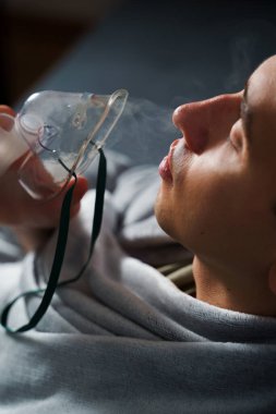 Evde hastalık tedavisi için kompresör nebulizatörü kullanılıyor. Öksürük tedavisi için oksijen maskesi takan bir adam.