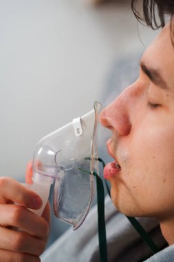 Evde hastalık tedavisi için kompresör nebulizatörü kullanılıyor. Öksürük tedavisi için oksijen maskesi takan bir adam.